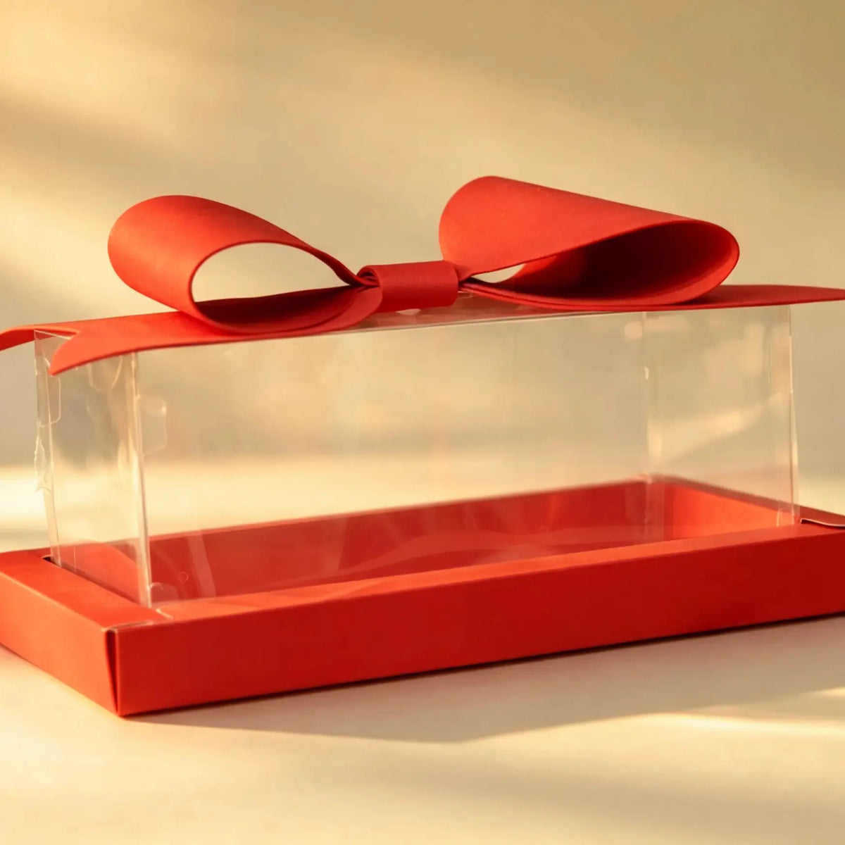 Clear PVC gift box with red tray base and red ribbon bow, front three-quarter view
