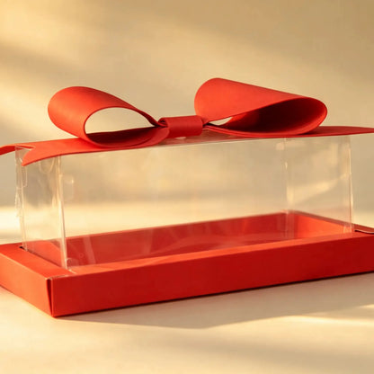 Clear PVC gift box with red tray base and red ribbon bow, front three-quarter view