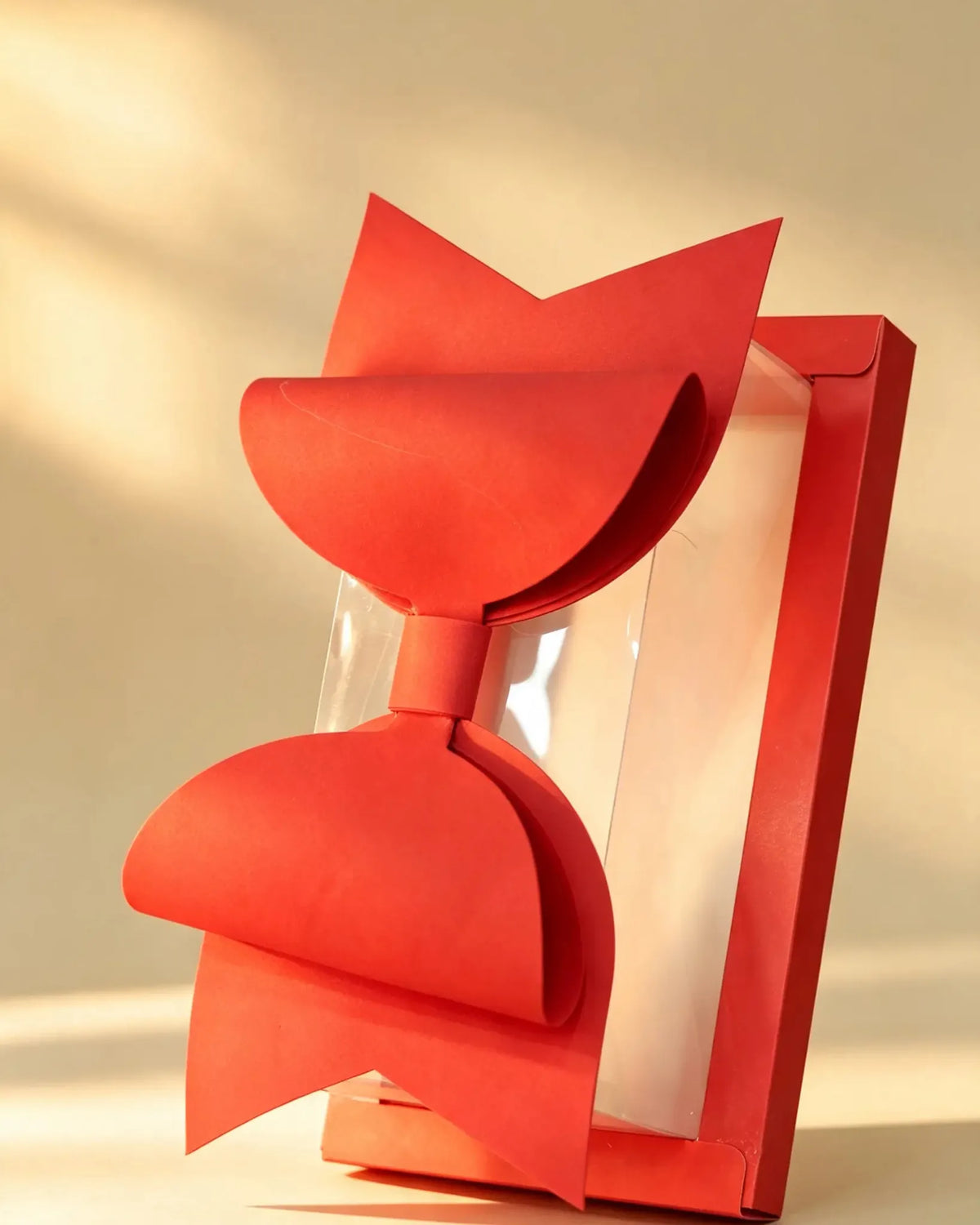 Clear PVC gift box tilted upright, showing red ribbon bow and transparent side panel