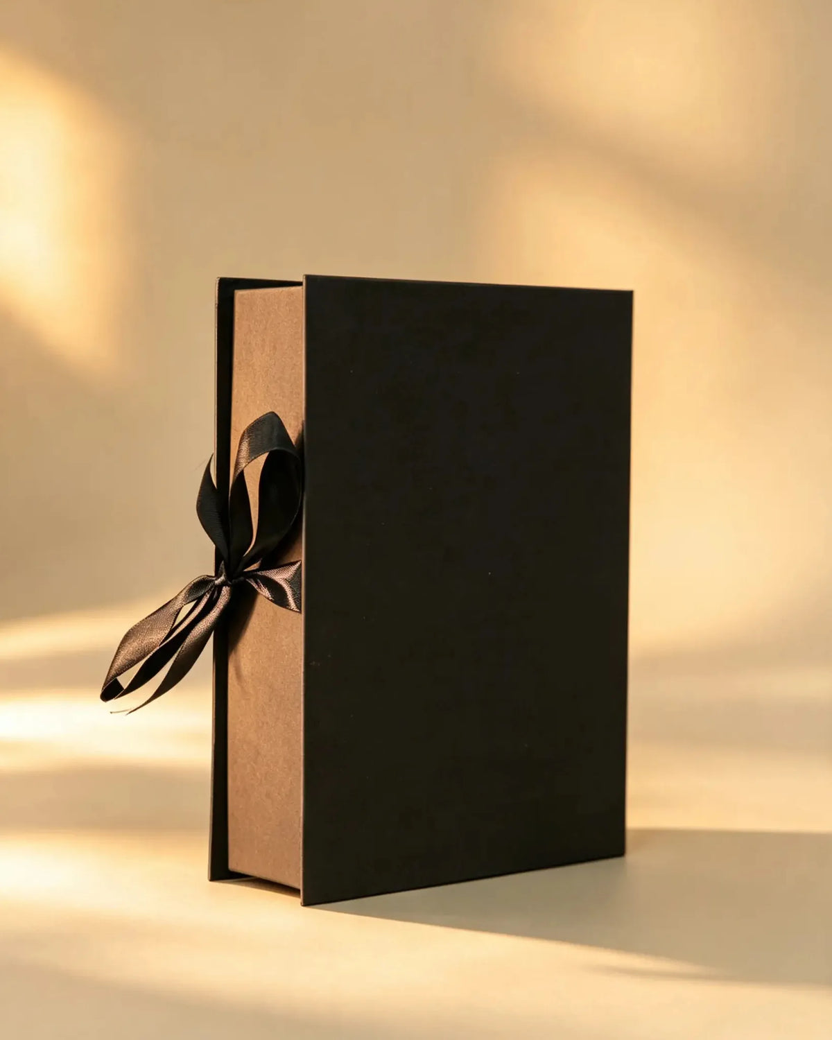 Black rigid gift box with kraft-brown edge and black ribbon bow, closed upright