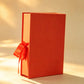 Red-orange rigid gift box with matching ribbon bow, closed upright