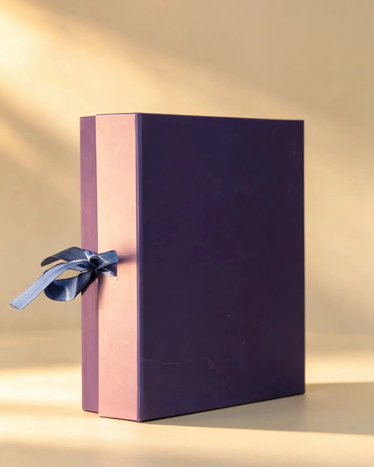 Purple and dusty rose two-tone gift box with blue ribbon bow, closed upright