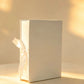 Ivory rigid gift box with a white satin ribbon bow, closed, front angle