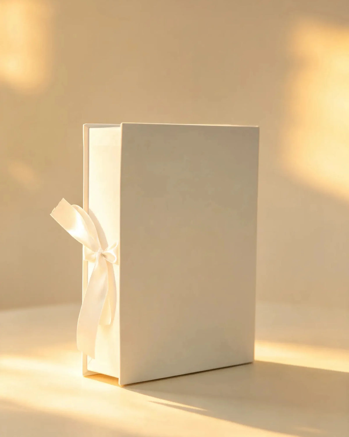 Ivory rigid gift box with a white satin ribbon bow, closed, front angle