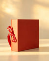 Rust red gift box with red satin ribbon bow, side angle view