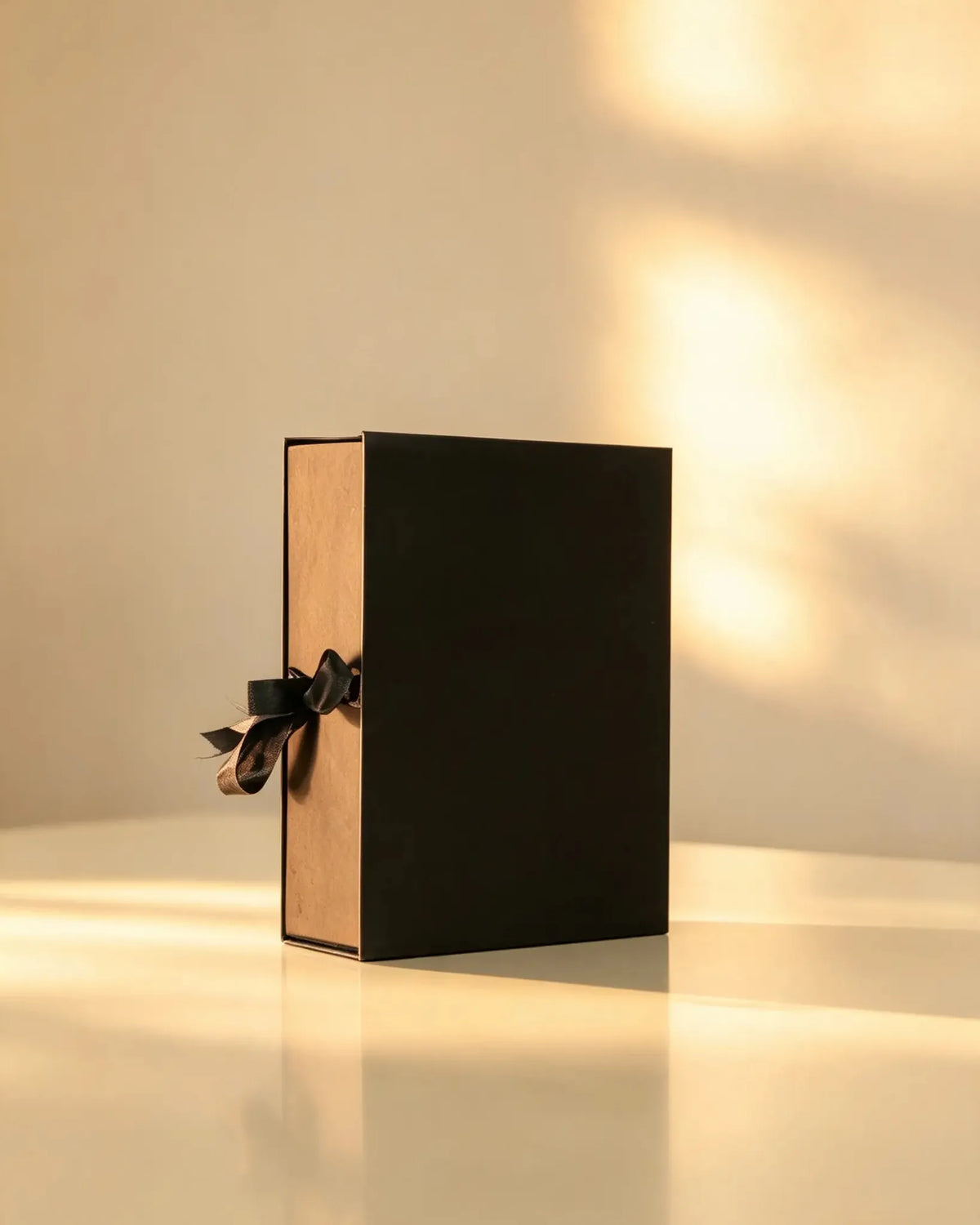 Black gift box with kraft-tone sides and black satin ribbon bow