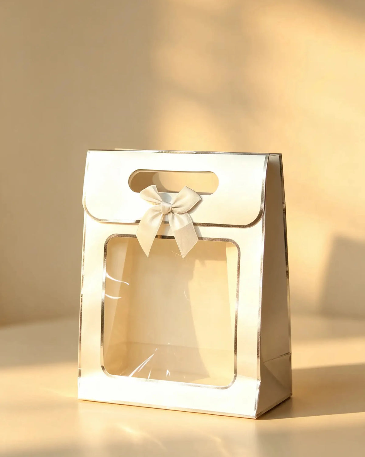 White pearlescent gift bag with silver foil trim, clear front window, and a cream ribbon bow